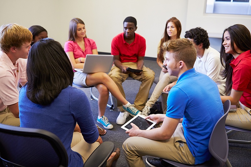 High school students and educator gathered in a circle with laptops and tablets